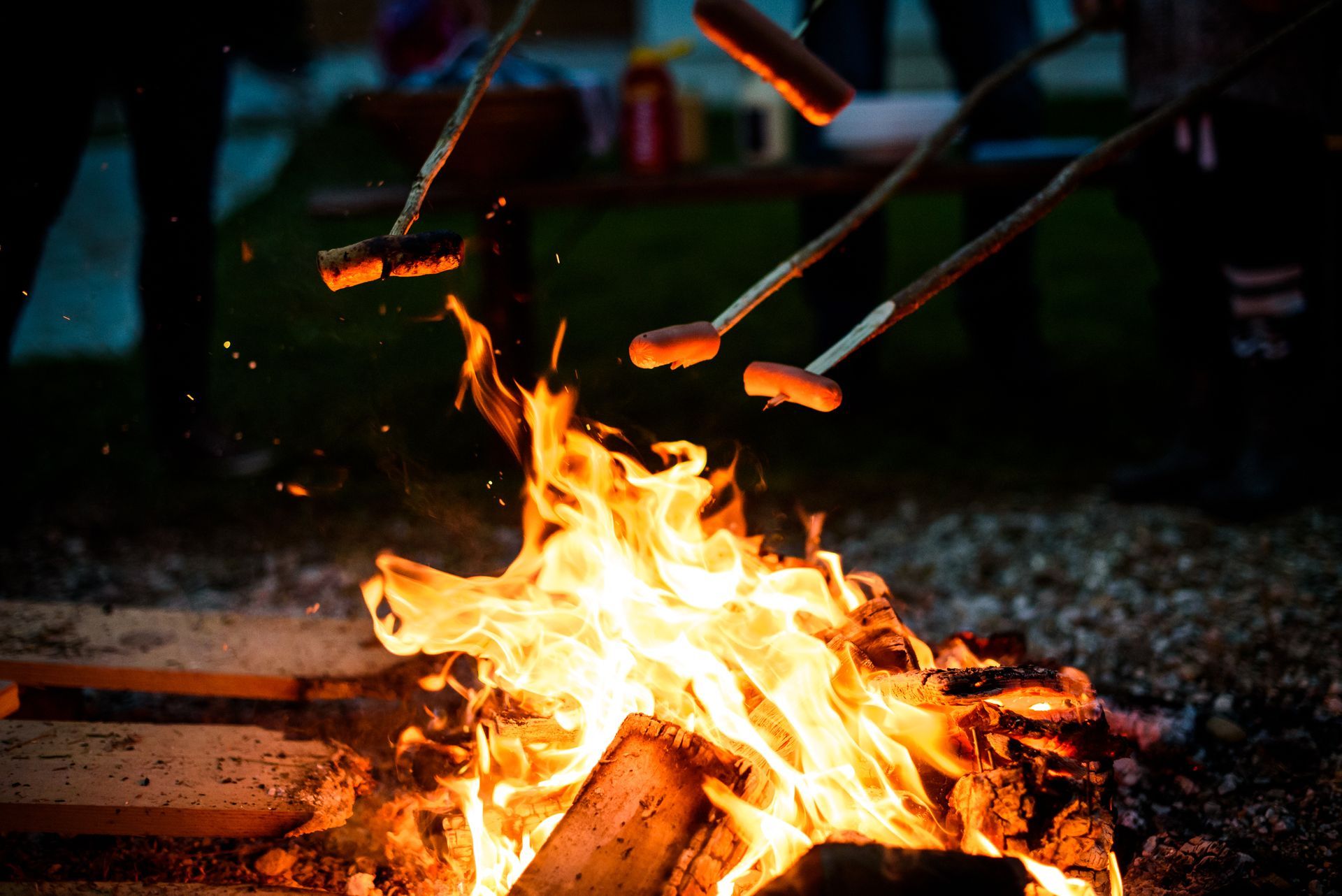 Campfire with burning flames, roasting sausages on sticks.