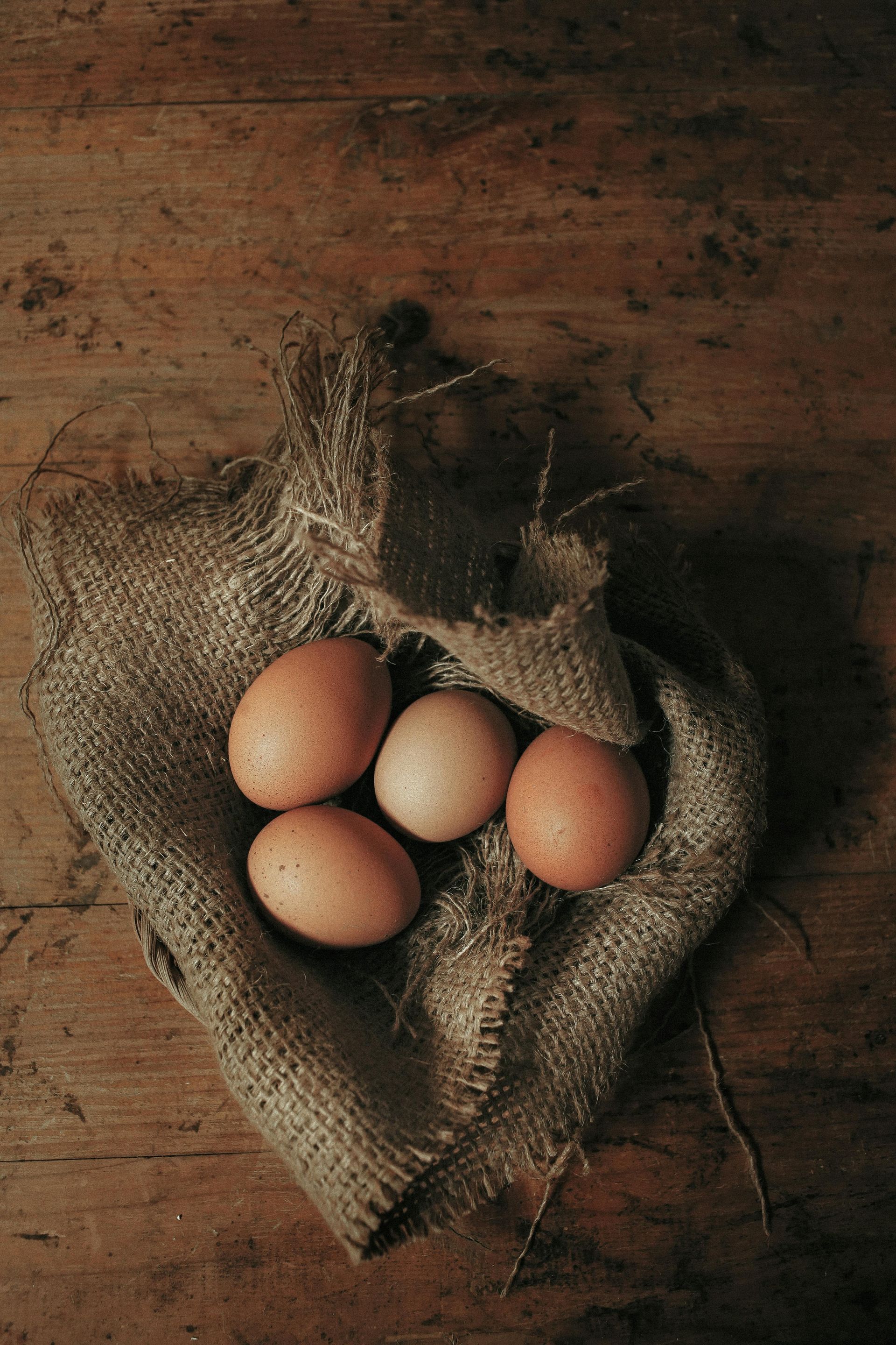 Five brown eggs nestled in a rustic burlap sack on a wooden table.