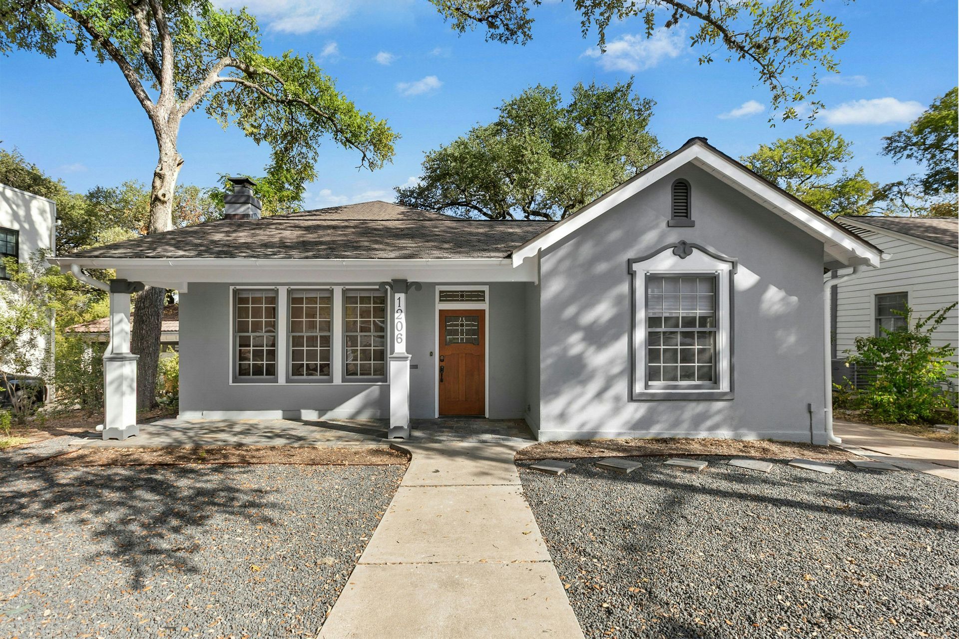 Gray house with wooden door and window, gravel yard, and concrete pathway.