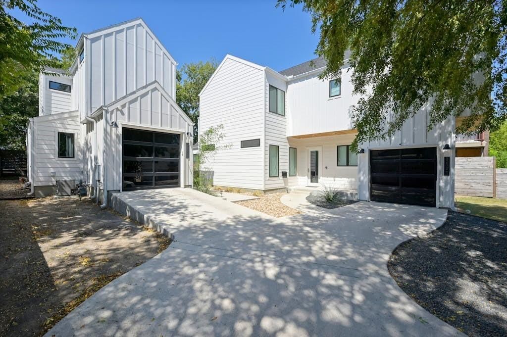 White modern houses with black garage doors and concrete driveways, under a sunny sky.