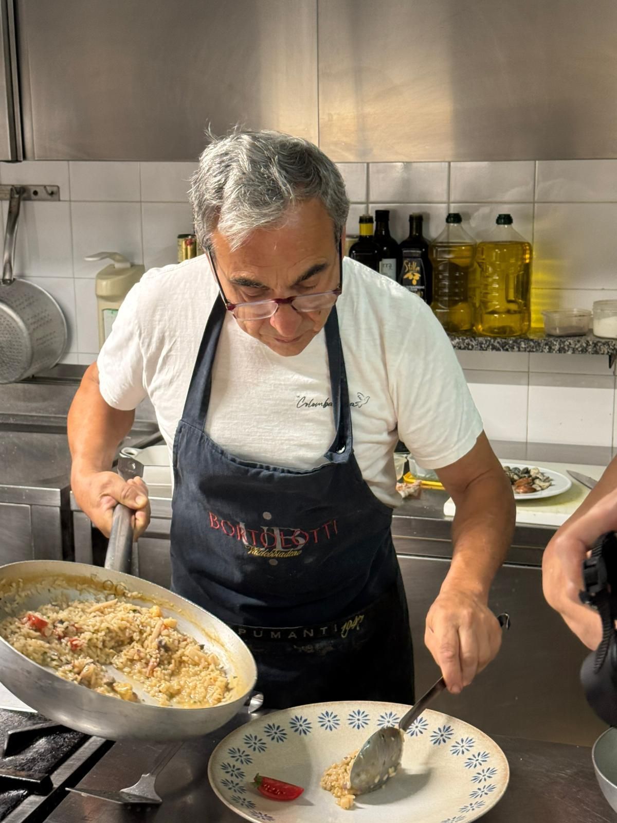 Uno chef in cucina serve il cibo da una grande padella a un piatto con un cucchiaio.