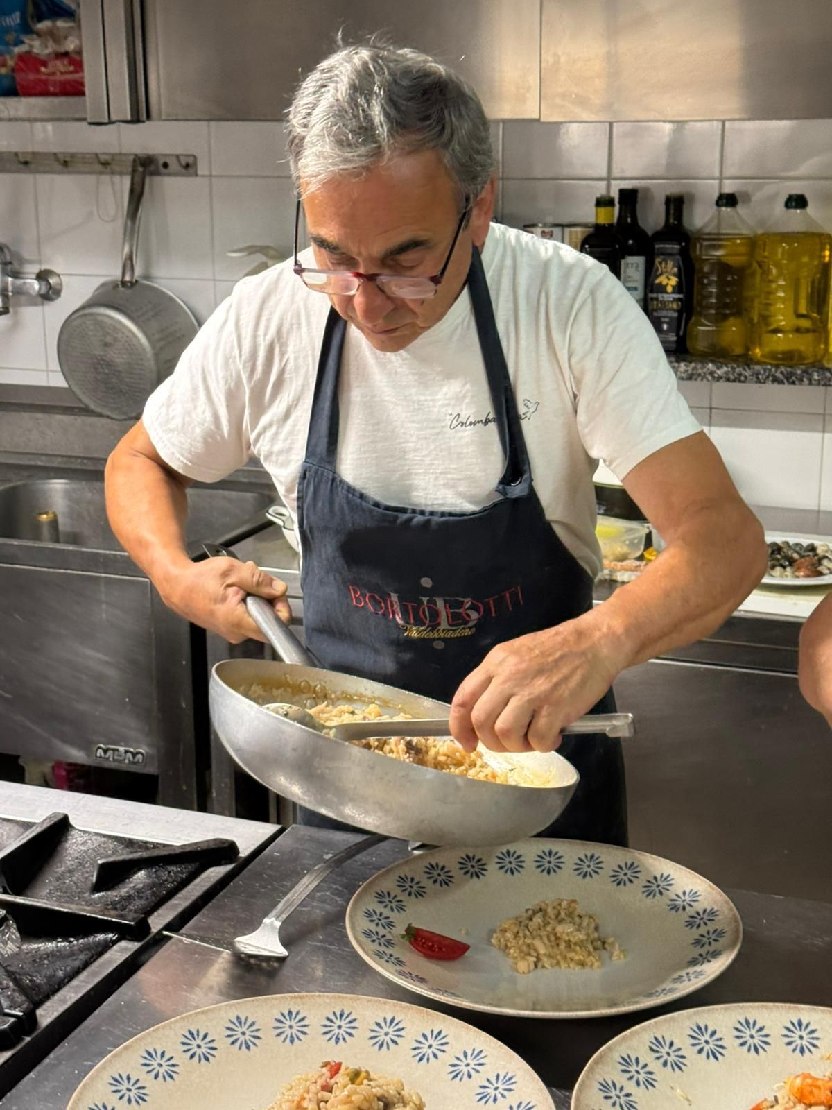 Uno chef impiatta in cucina, tenendo una padella sopra un piatto decorato.