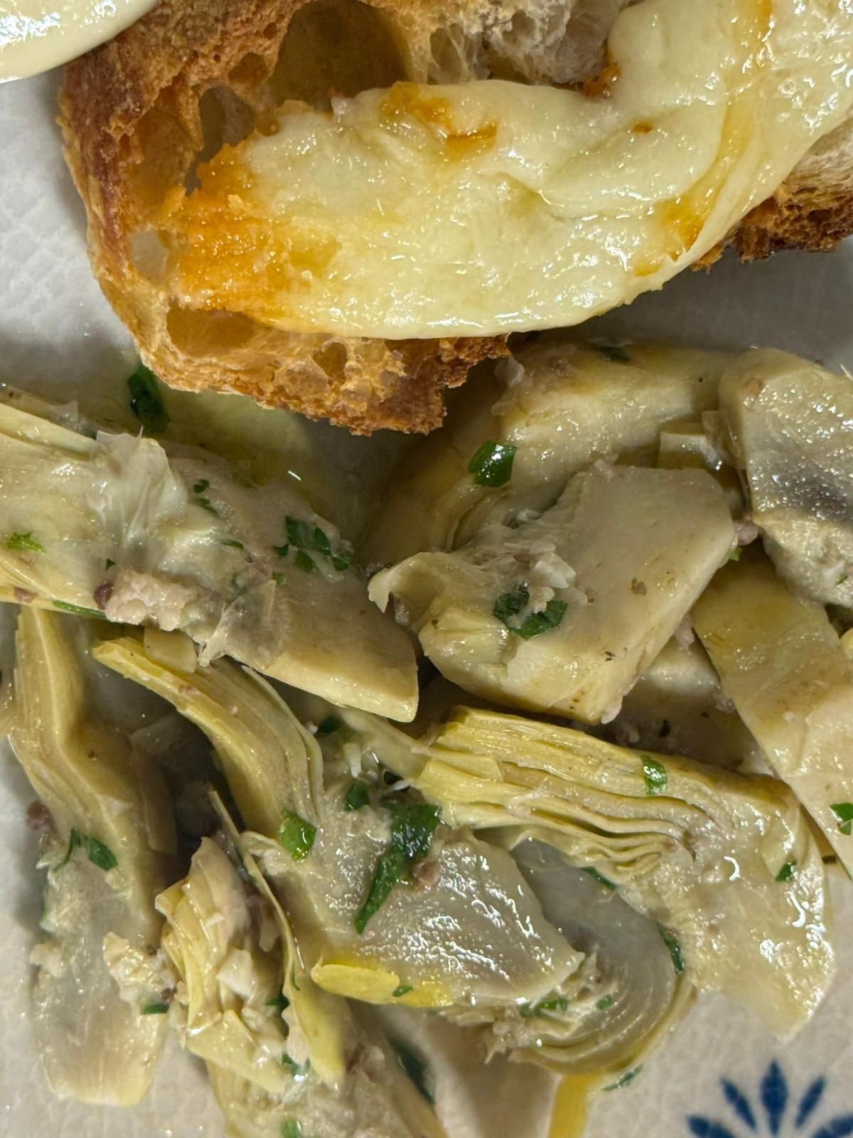 Primo piano di cuori di carciofo cremosi su un piatto, con una fetta di pane sopra.
