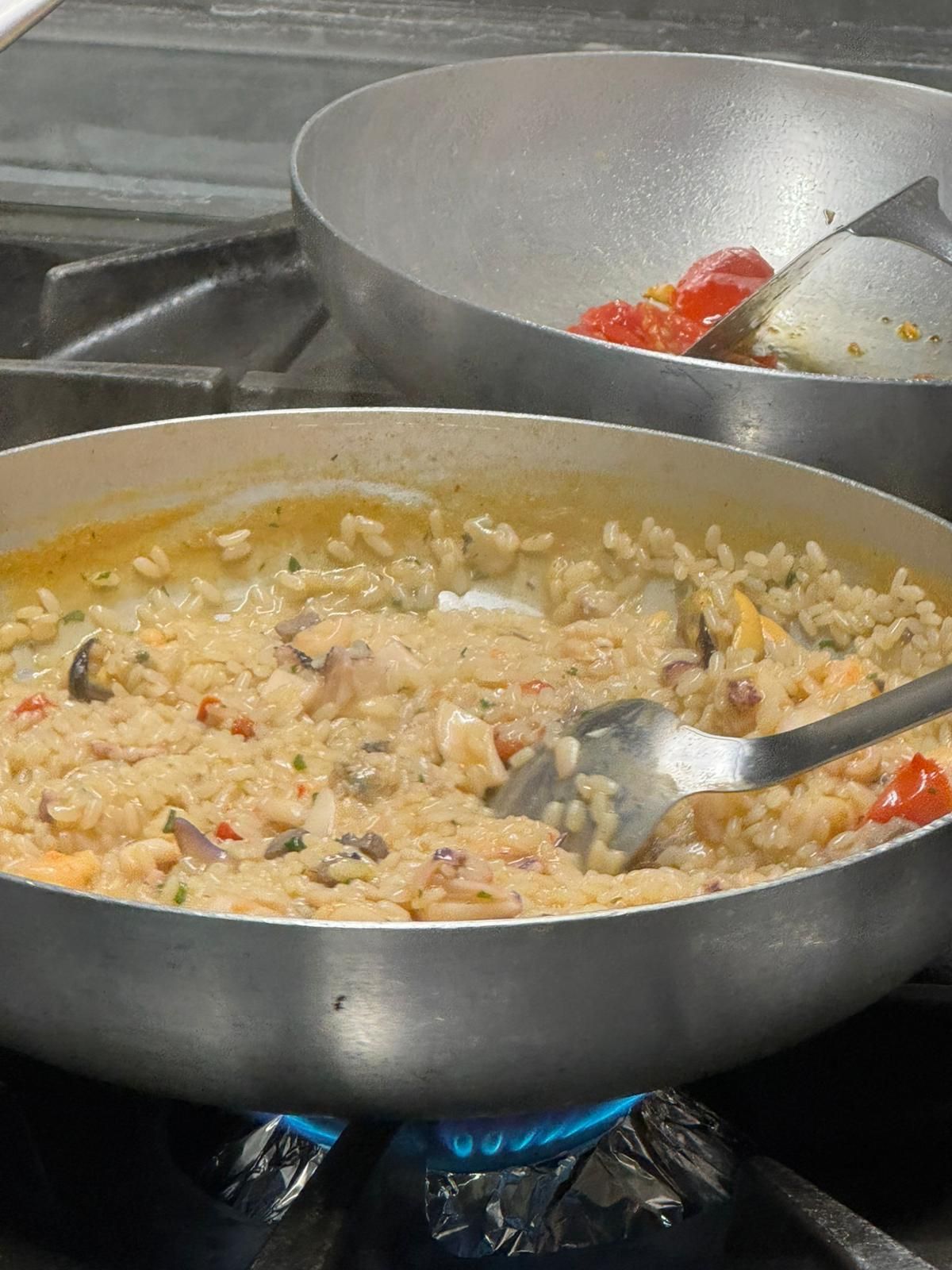 Due pentole di riso cremoso stanno cuocendo su un fornello a gas, una delle quali viene mescolata con un cucchiaio.