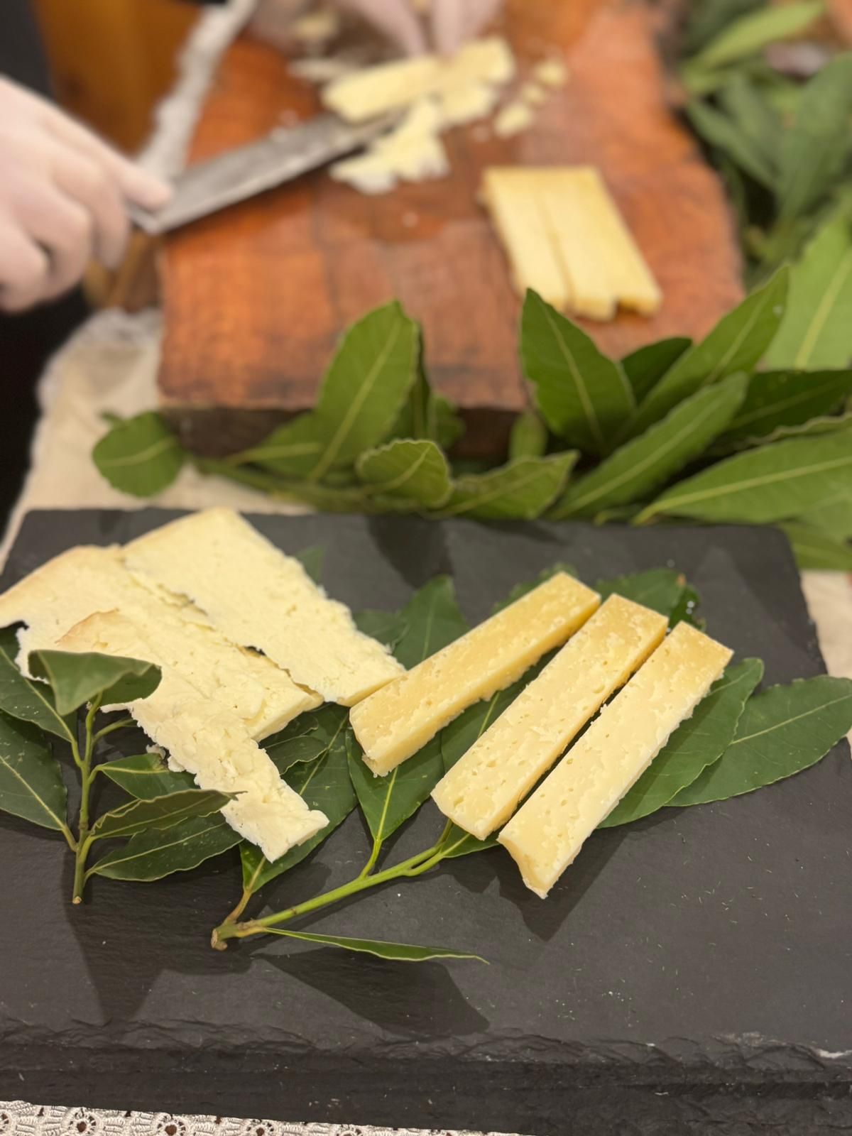 Piatto di formaggi con erbe aromatiche, fette di formaggio e pane su taglieri di ardesia scura.