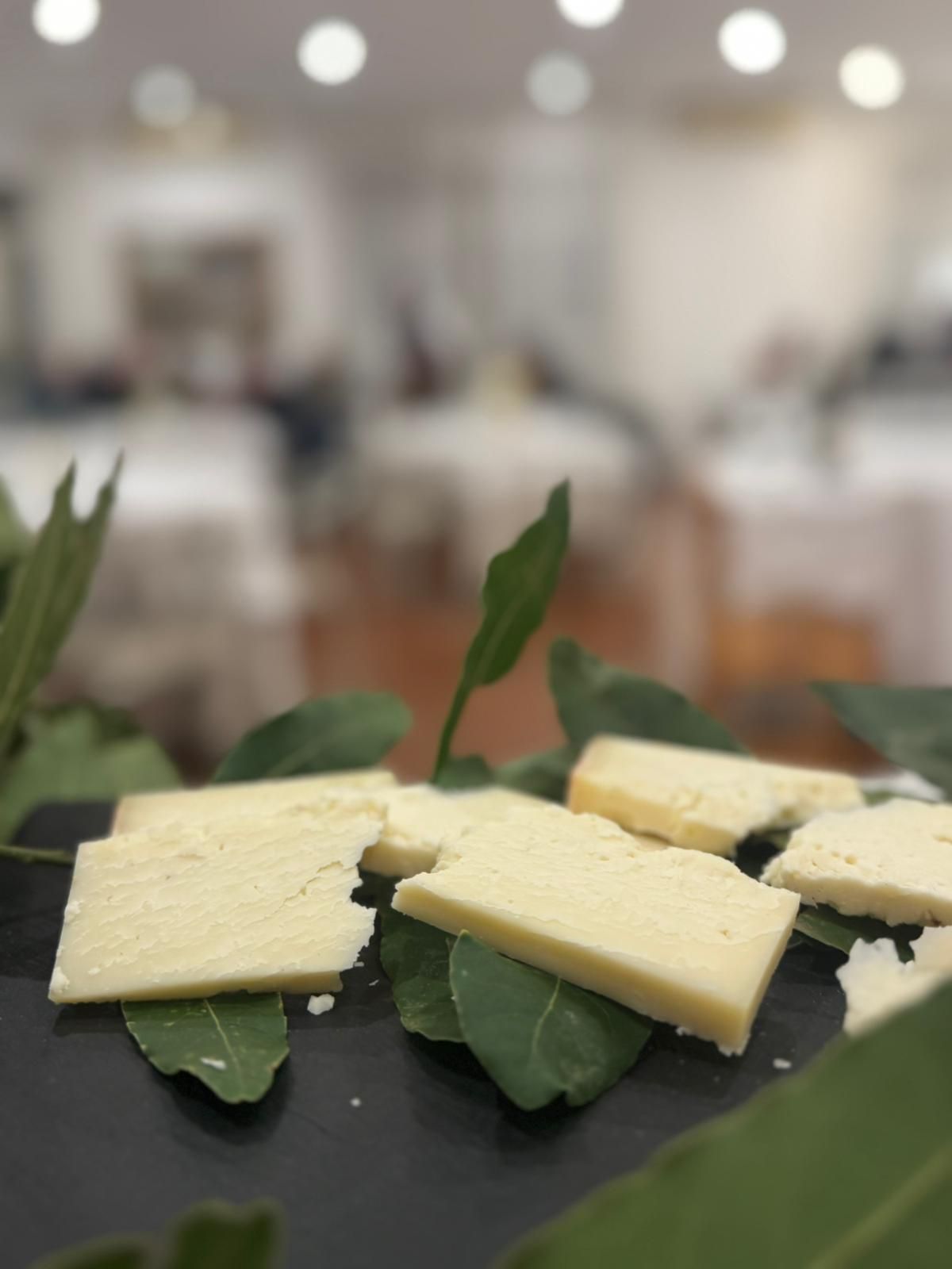 Fette di formaggio su un piatto scuro con foglie verdi, servite su un tavolo in un'ambientazione sfocata di un ristorante.