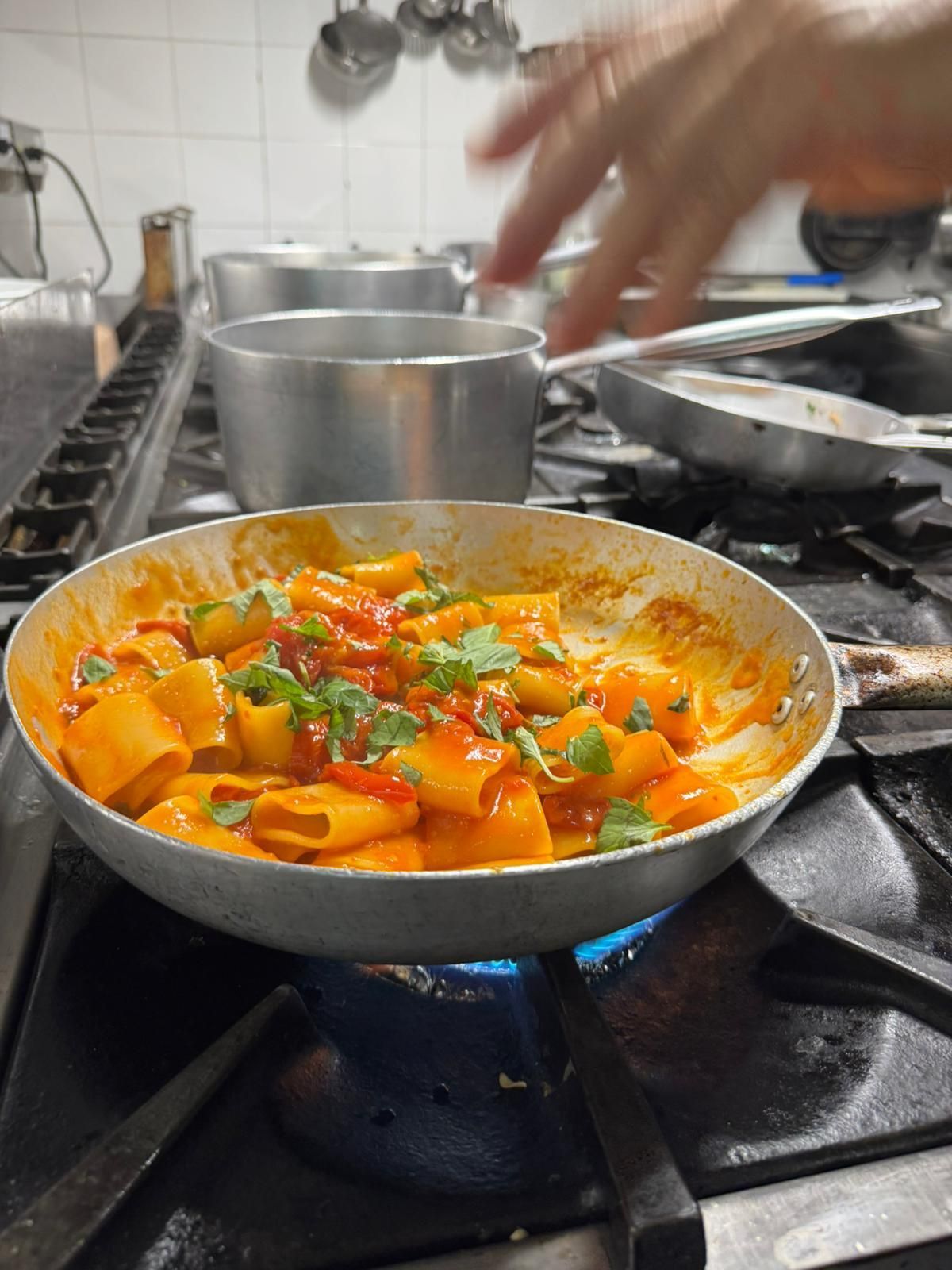 Verdure arancioni che sobbollono in una padella su un fornello a gas, guarnite con erbe aromatiche, in una cucina