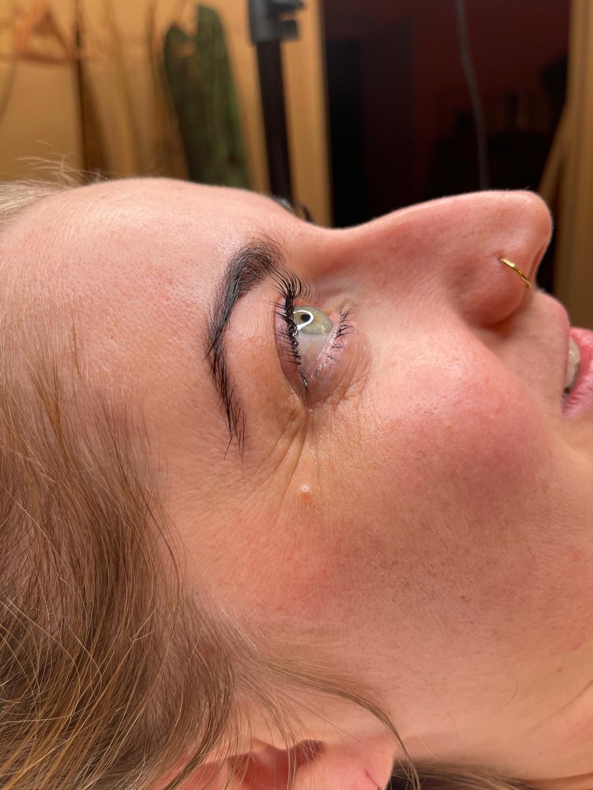 Nahaufnahme eines Gesichts im Profil mit goldenem Nasenring und tropfenförmigem Lippenstift auf der Wange.