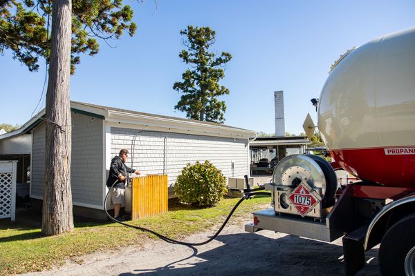 Newport Propane driver running a delivery hose from a propane truck to a customer's tank