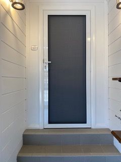 A door with a screen on it is in a hallway next to stairs — Plantation Shutters in Singleton, NSW