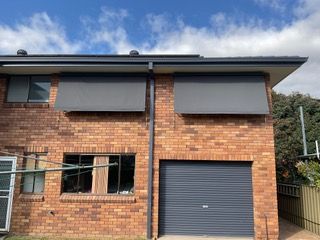 A brick house with a garage and a gray awning on the windows — Plantation Shutters in Singleton, NSW