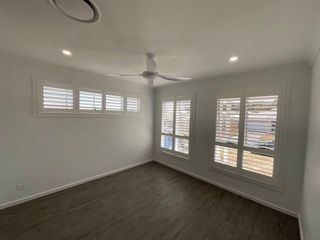 An empty room with a ceiling fan and shutters on the windows — Plantation Shutters in Singleton, NSW