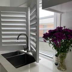 A kitchen with a sink and a vase of purple flowers — Plantation Shutters in Singleton, NSW