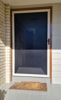 A screen door with a welcome mat on the porch of a house — Plantation Shutters in Singleton, NSW