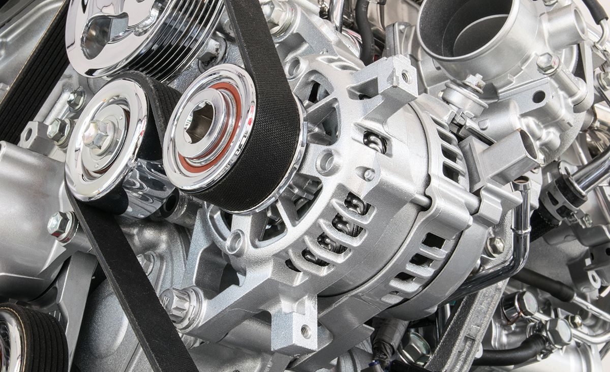 Close-up of a car engine with belts, pulleys, and alternator, showing metallic silver components.