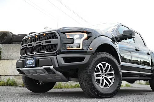 A low-angle shot of a black Ford Raptor truck parked outdoors with a silver skid plate and large off-road tires.
