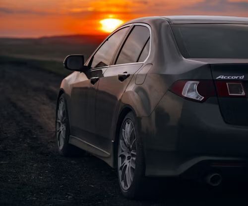 Dark grey sedan parked on a dirt road at sunset.