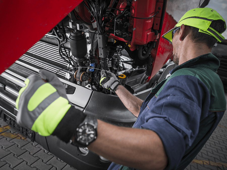 A man wearing a yellow hat and gloves is working on a truck.