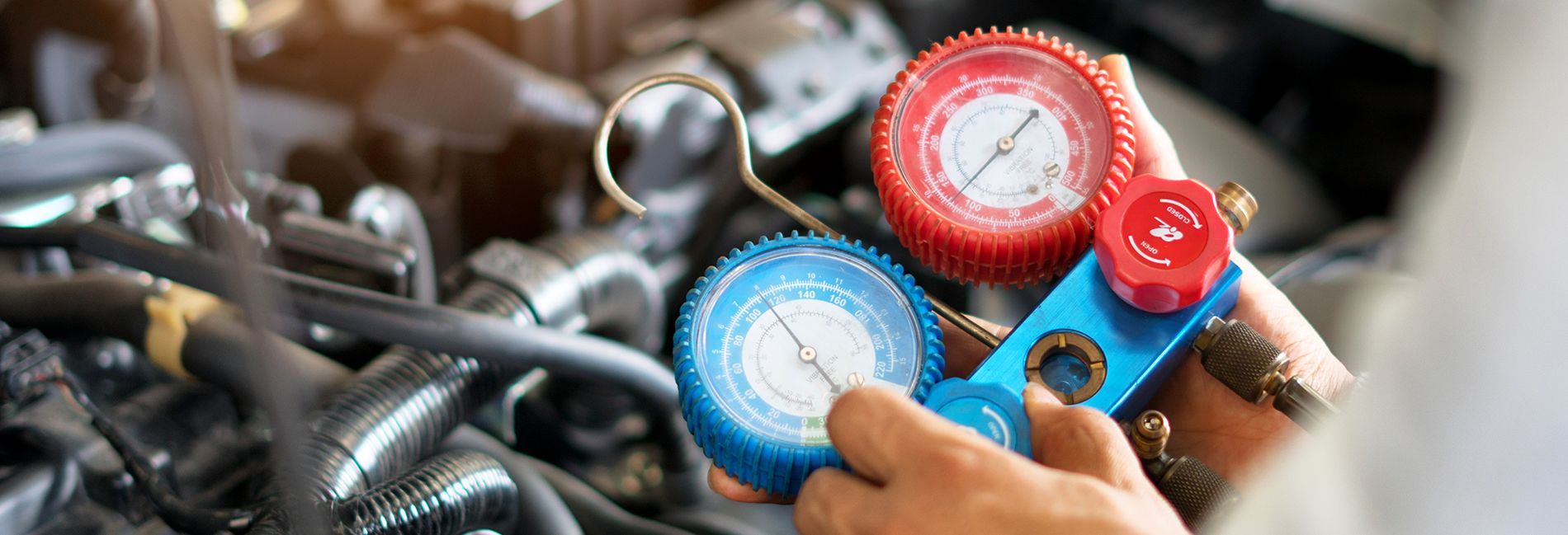 Close-up of a person holding gauges near car engine, checking the air conditioning system.