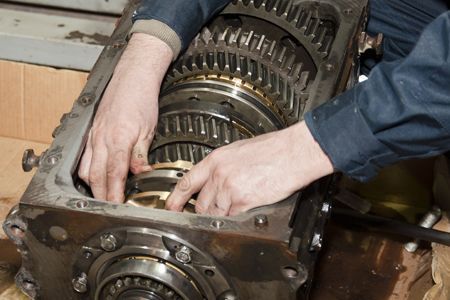 Hands working on a complex gear system inside a metal casing.