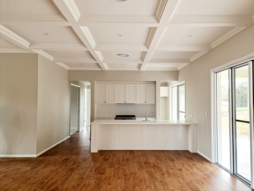 An empty room with hardwood floors and a kitchen in the background.