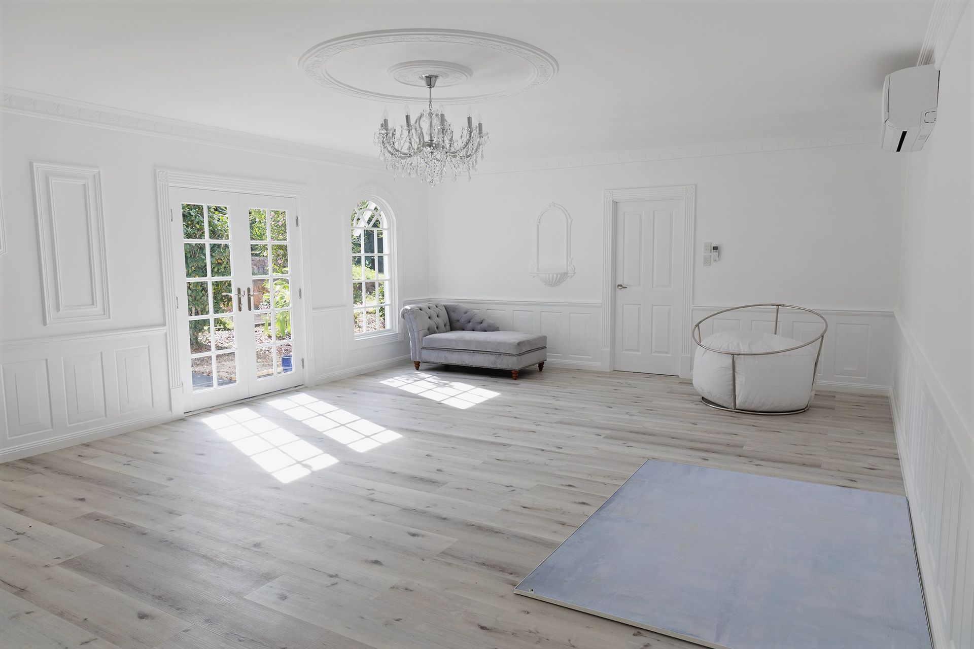 An empty room with white walls , wooden floors , a couch and a chandelier.