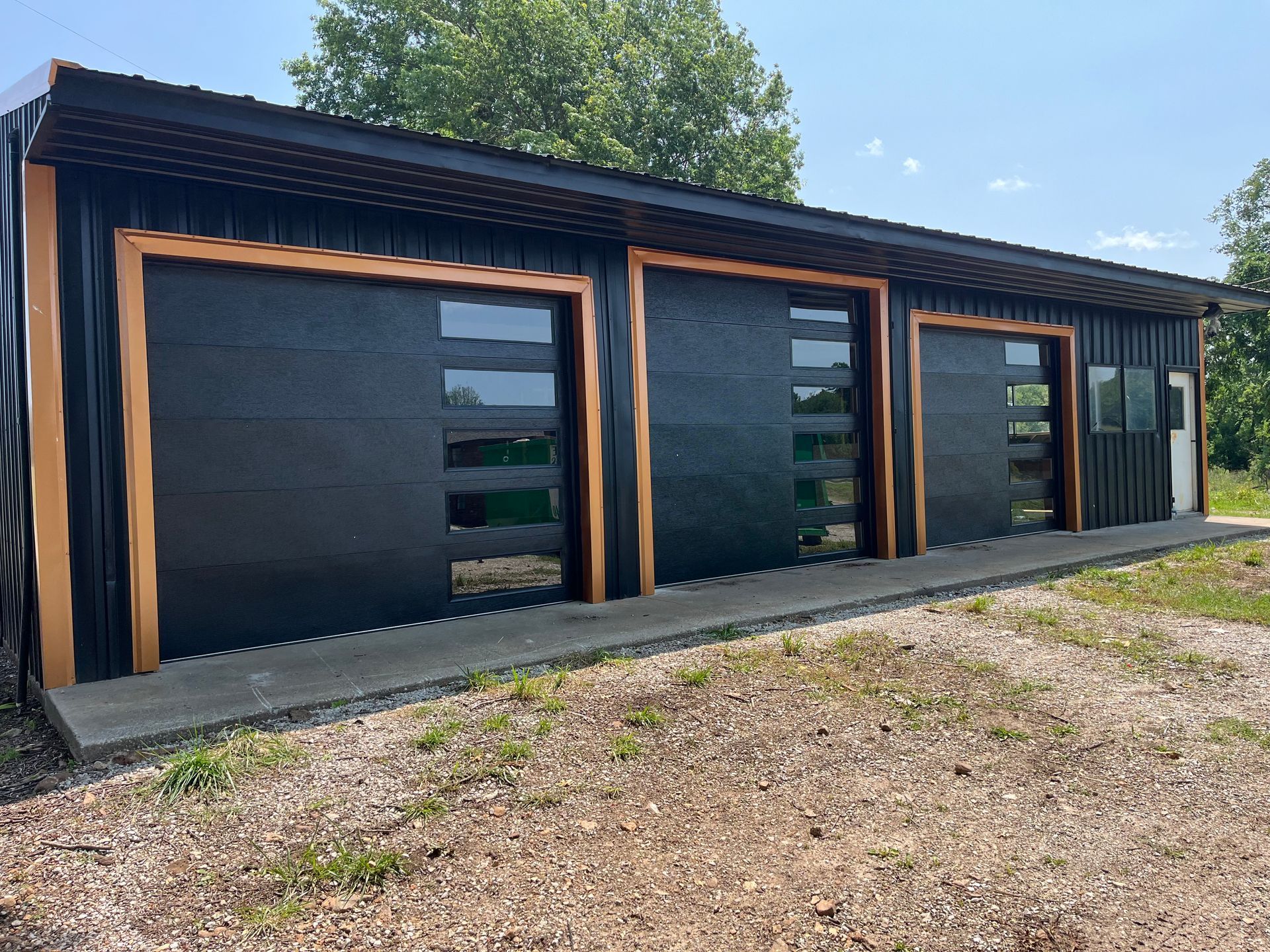 A white metal building with a single-car garage door and a separate side entry door, viewed from a gravel driveway.