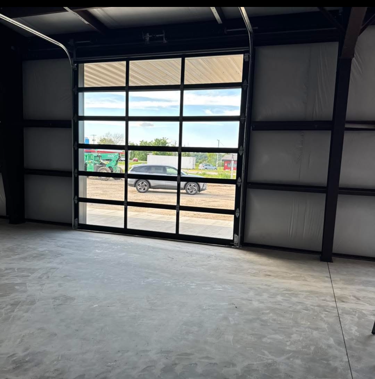 Interior view of an industrial space featuring a large glass-paneled garage door looking out onto a parking lot and sky.
