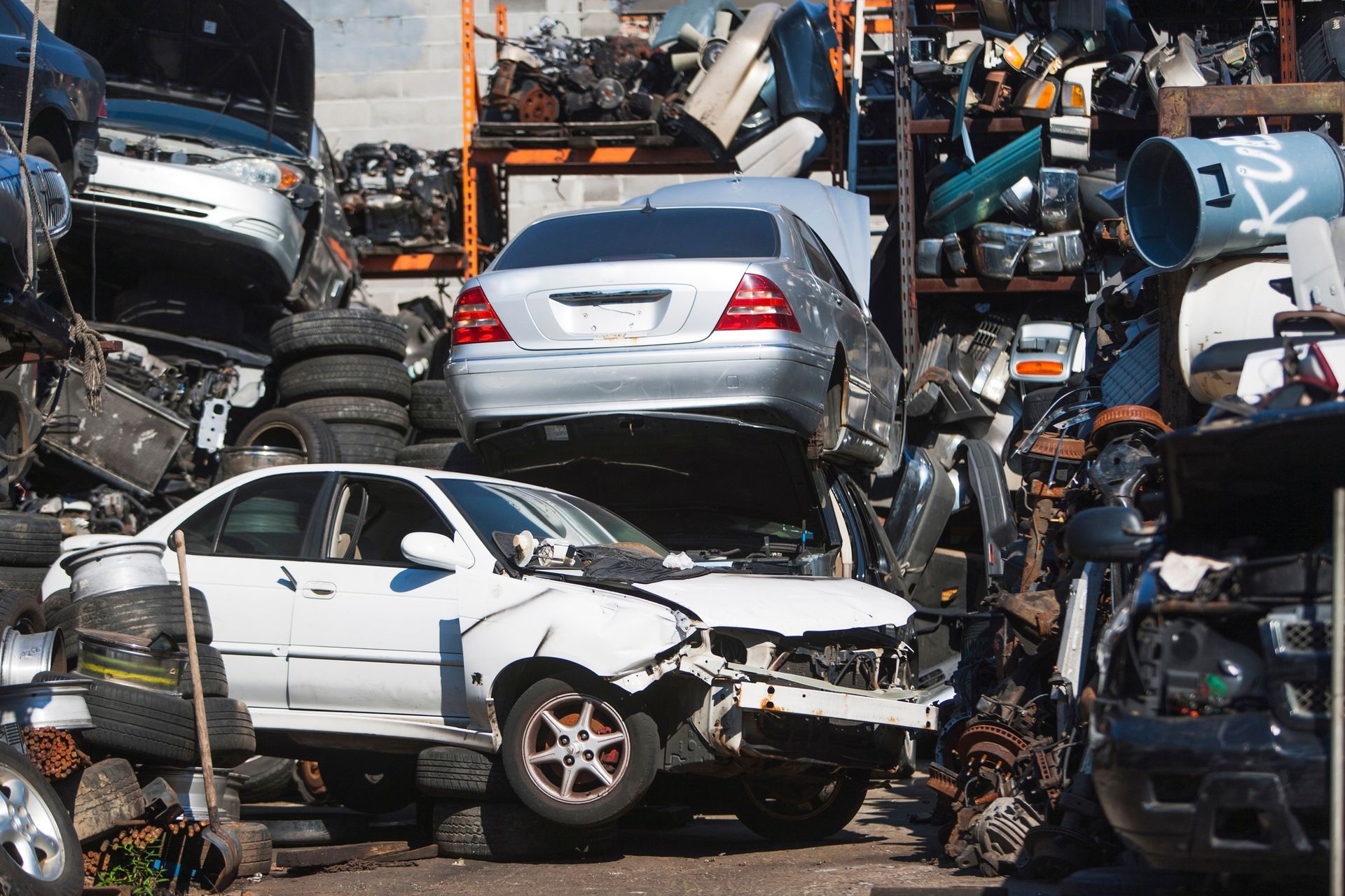 Stacked wrecked cars and scattered parts fill a crowded salvage yard.