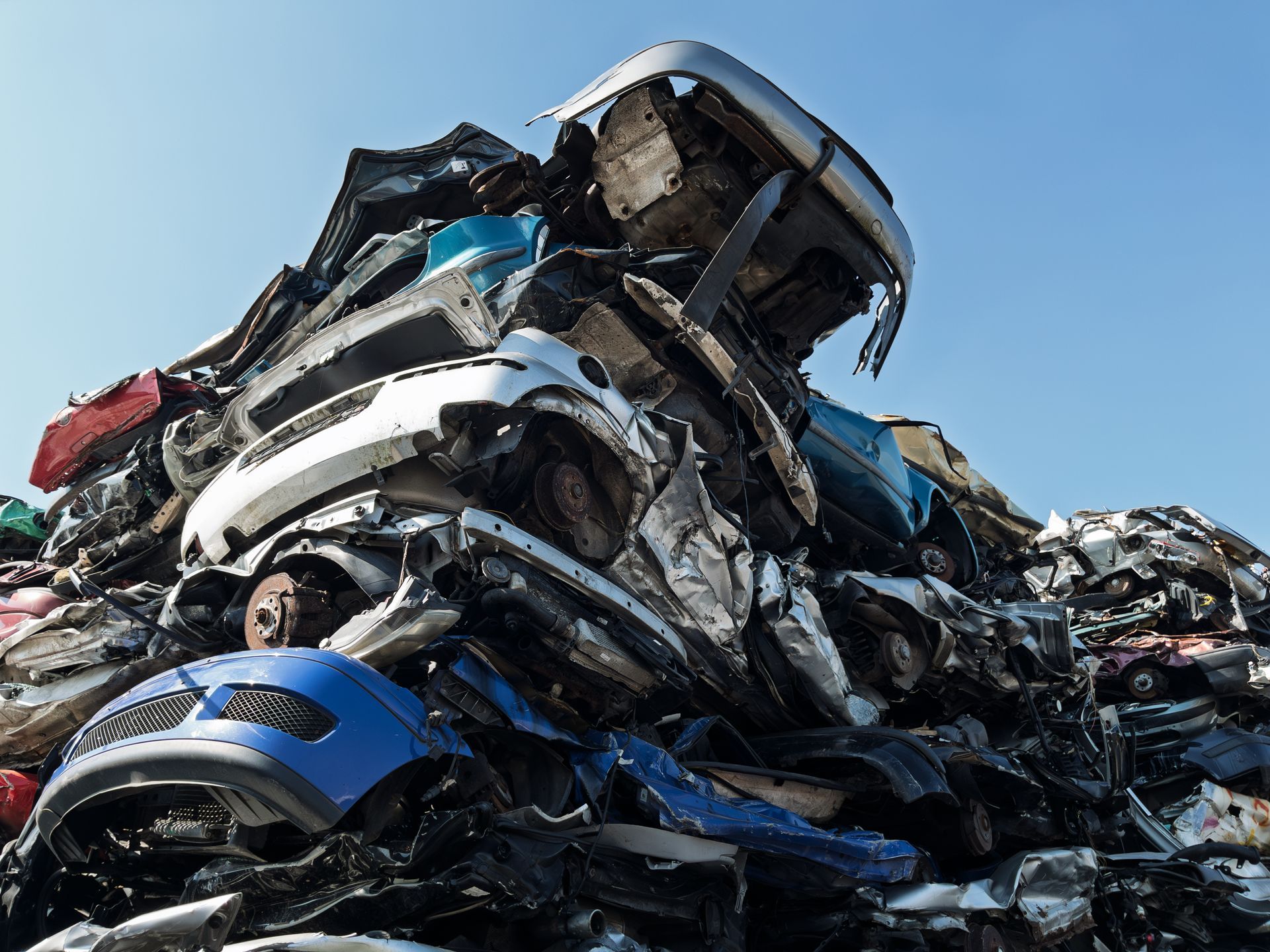 Stacked wrecked cars at auto salvage yard, damaged vehicles piled for recycling and used parts sales.