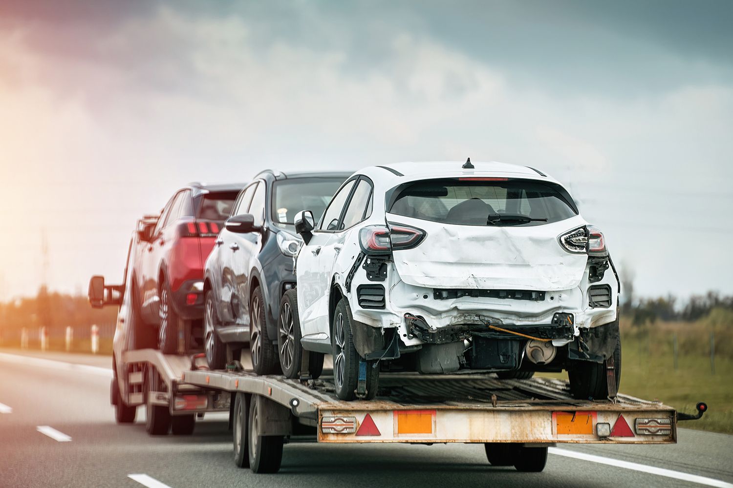 Damaged vehicles on tow truck representing cash for junk cars from total loss cars.