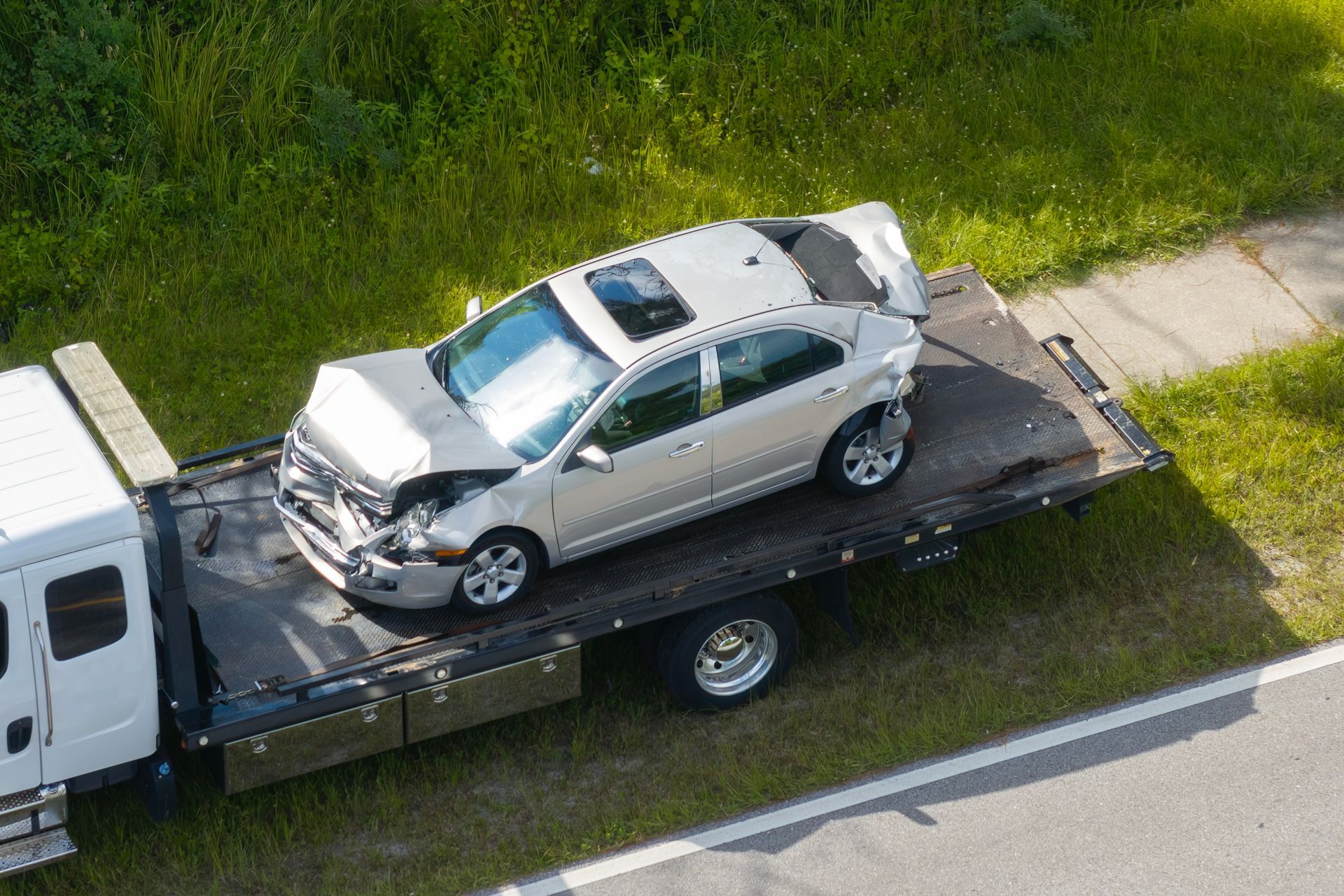Silver SUV with front-end damage on a flatbed tow truck beside a road