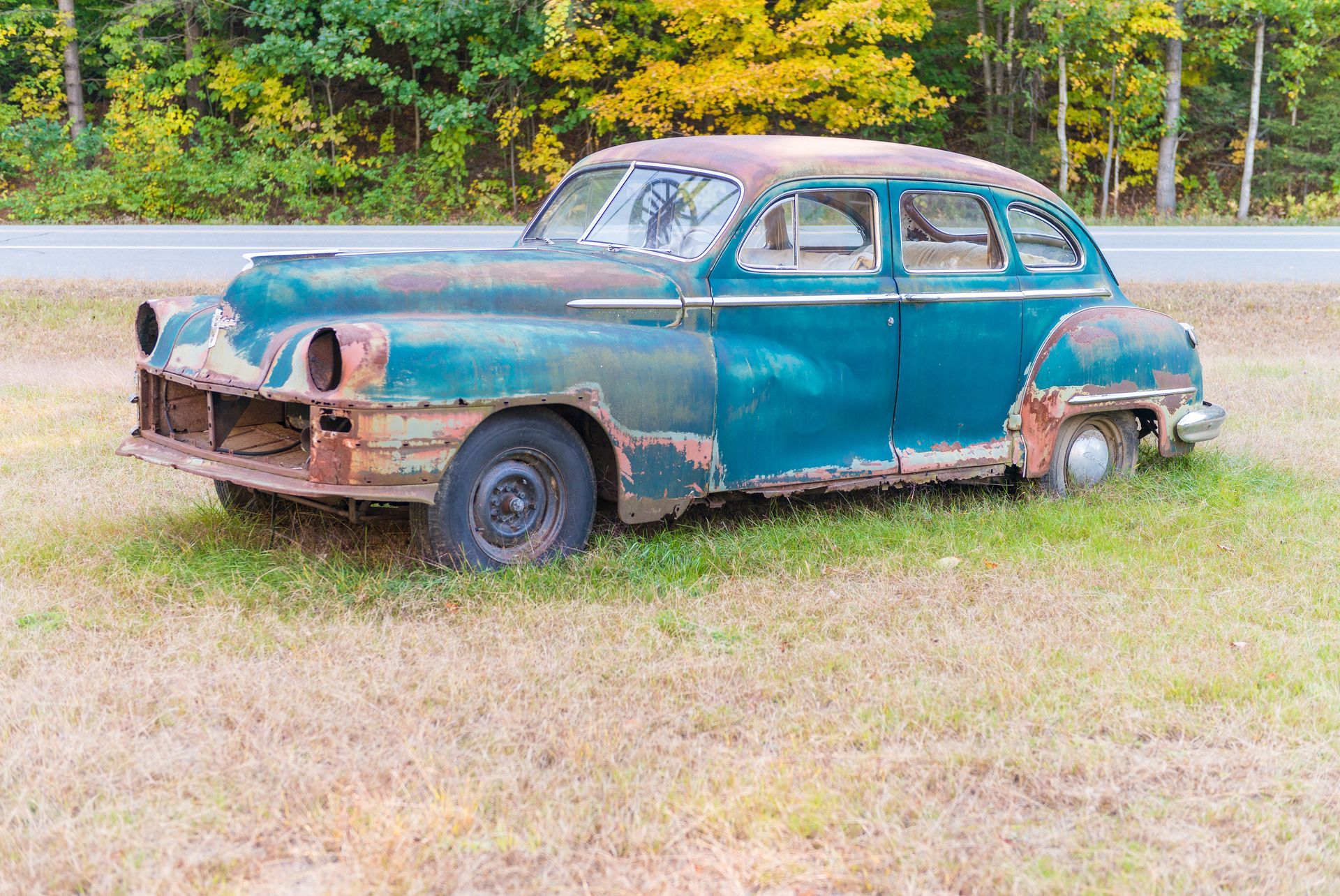 Rusty vintage car missing parts in a grassy field beside a road. Rusty vintage car missing parts in a grassy field beside a road.