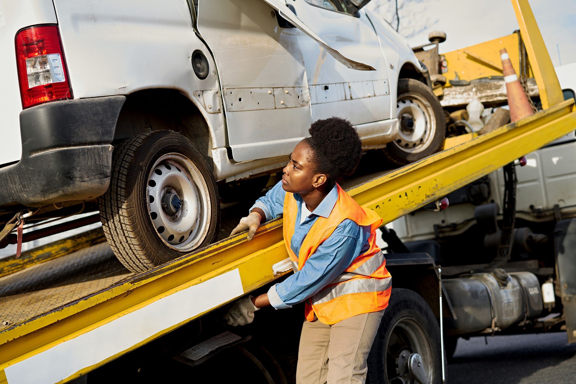 Towing operator managing a junk car on a flatbed truck.