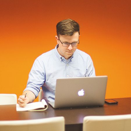 A man is taking notes while attending a webinar on his laptop.