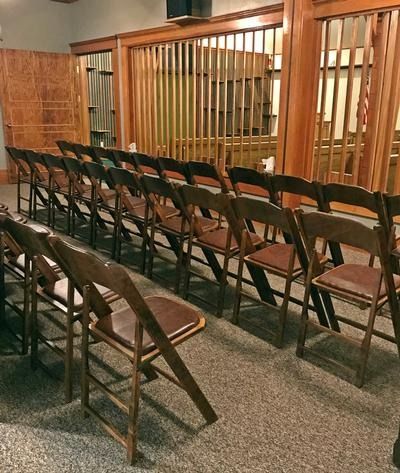 Rows of wooden folding chairs arranged in a room with a wooden slatted divider separating the seating area.