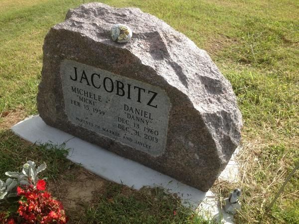 A rustic granite headstone for the Jacobitz family, featuring the names Michele and Daniel, set in a grassy cemetery.