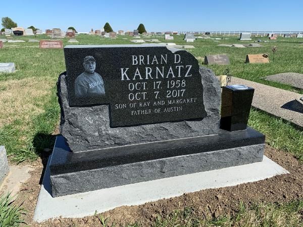 A black granite headstone for Brian D. Karnatz, Oct 17 1958–Oct 7 2017, featuring his portrait in a cemetery setting.