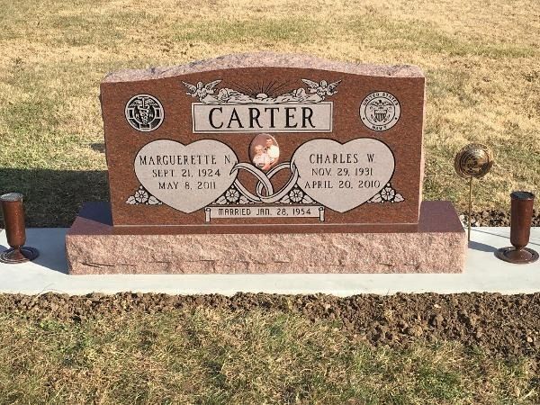 A granite headstone for the Carter family, featuring names, dates, and two heart-shaped engravings on a cemetery lawn.