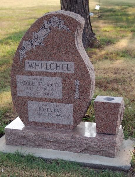 A teardrop-shaped red granite tombstone for the Whelchel family, featuring floral engravings and a side vase.