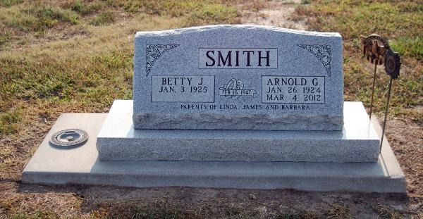 A grey granite headstone for Betty J. and Arnold G. Smith, set in a grassy cemetery, displaying names and dates.