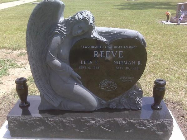 A heart-shaped granite gravestone featuring a sculpted figure and the inscription 
