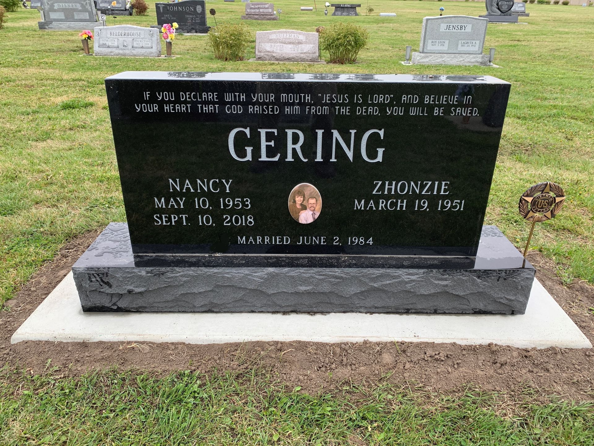 A black granite Gering family headstone with a central photo, names, and dates, situated in a grassy cemetery.