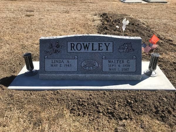 A grey granite gravestone for the Rowley family, situated in a cemetery, featuring two markers and flanking metal vases.