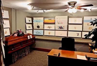 A funeral showroom with a casket, a desk with a chair, and wall-mounted displays of various memorial plaque designs.