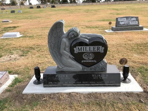 A dark granite heart-shaped gravestone with an angel carving, marked 