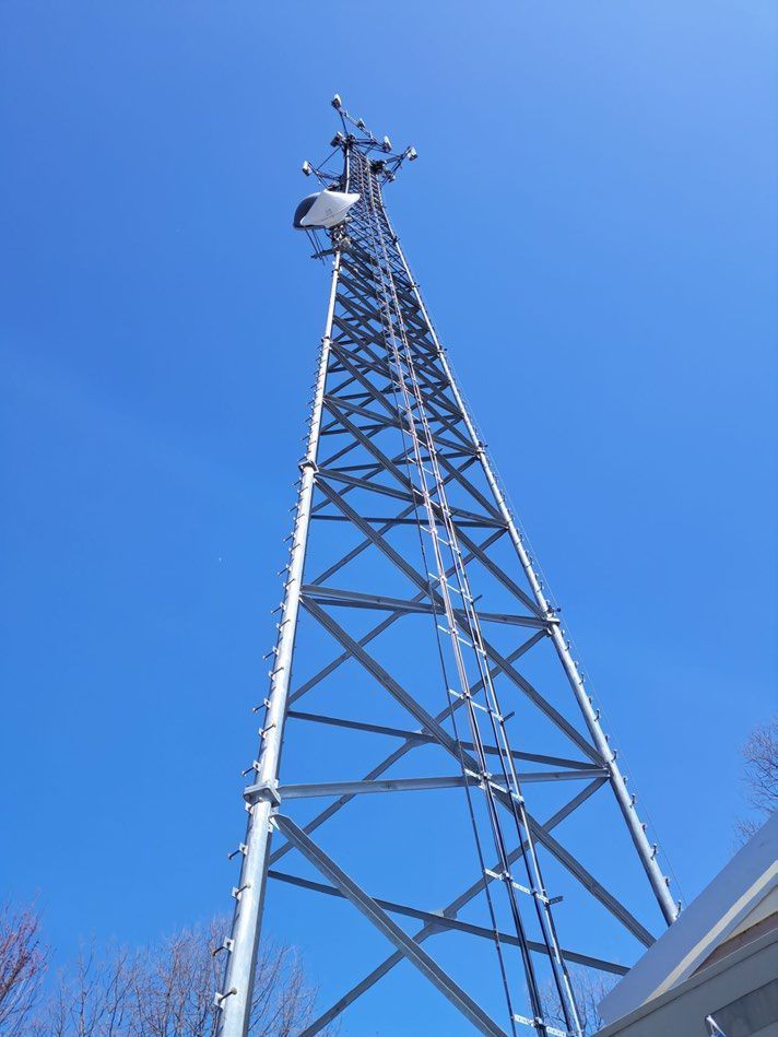 A telephone tower with antennas against a blue sky at sunset.