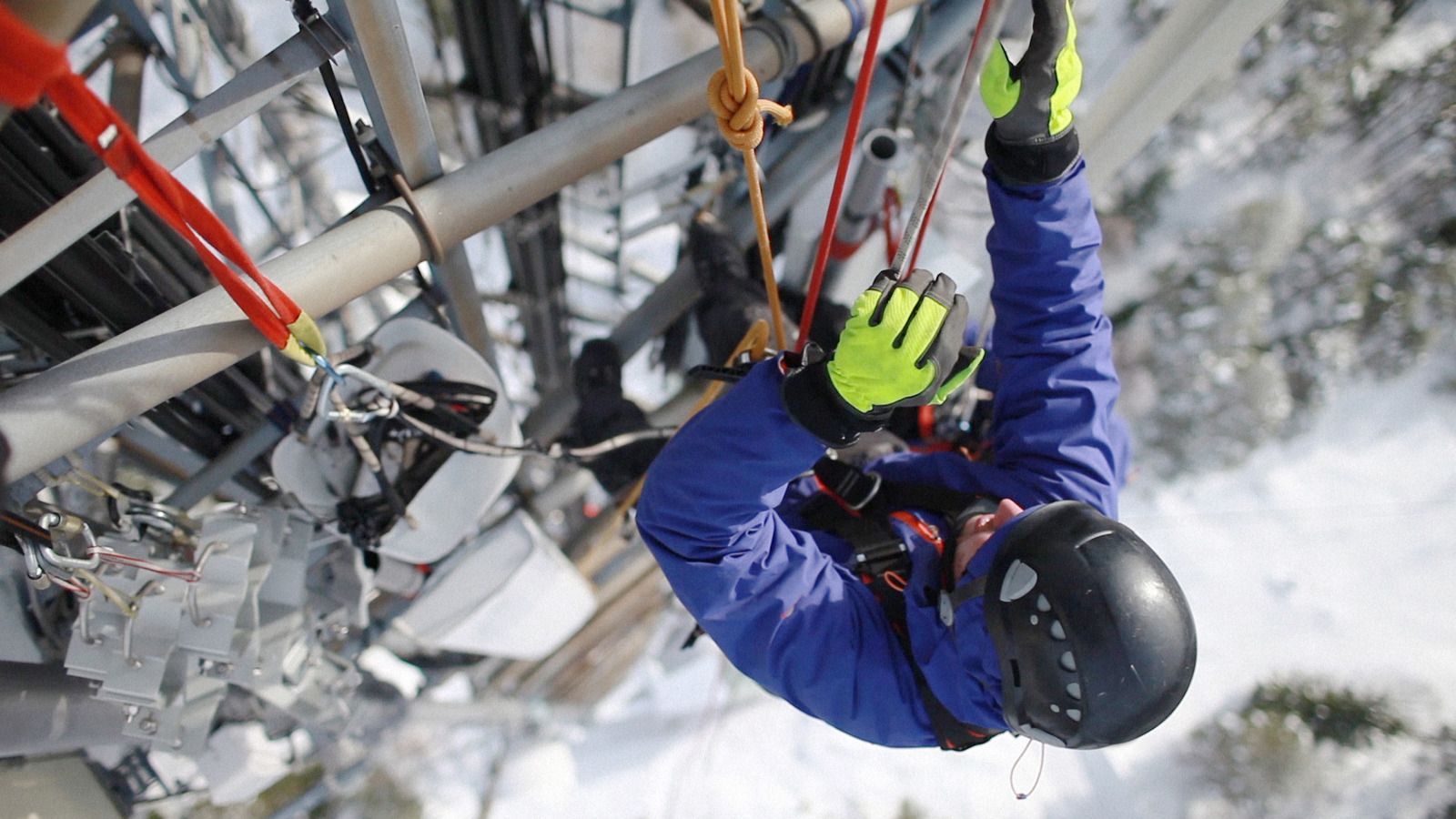A man wearing a helmet and gloves is hanging upside down from a pole.