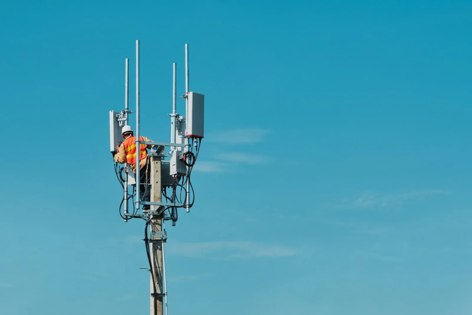 A man is standing on top of a cell phone tower.