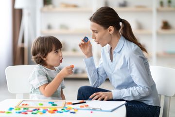 Woman and child playing with colorful shapes, likely in a therapy session.